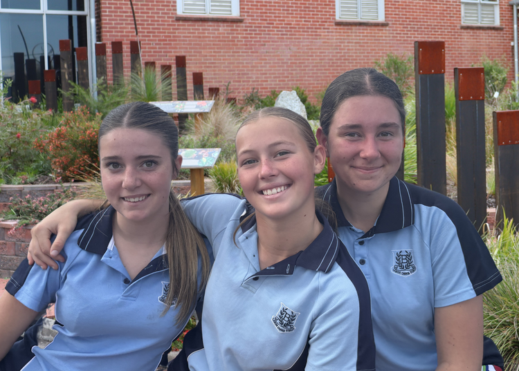Image of three smiling students standing in the gardens in front of Bega High School.