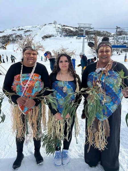 Image of 3 aborignal women dressed in traditional aboriginal grass skirts and headwear, holding bunches of eucatlyptus leaves standing in the snow.