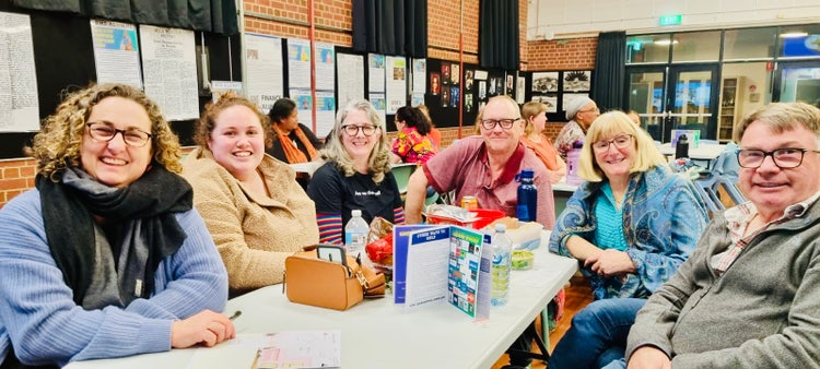 Image of a group of smiling people seated around a table with trivia items placed between them.